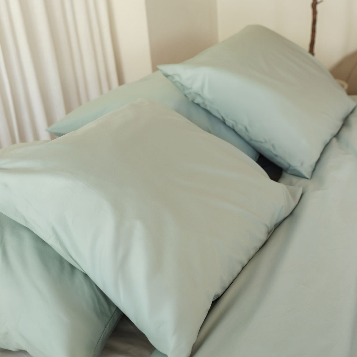 Plumelle pillowcase in Sage on a neatly made bed with matching bedding in a bright minimalist bedroom