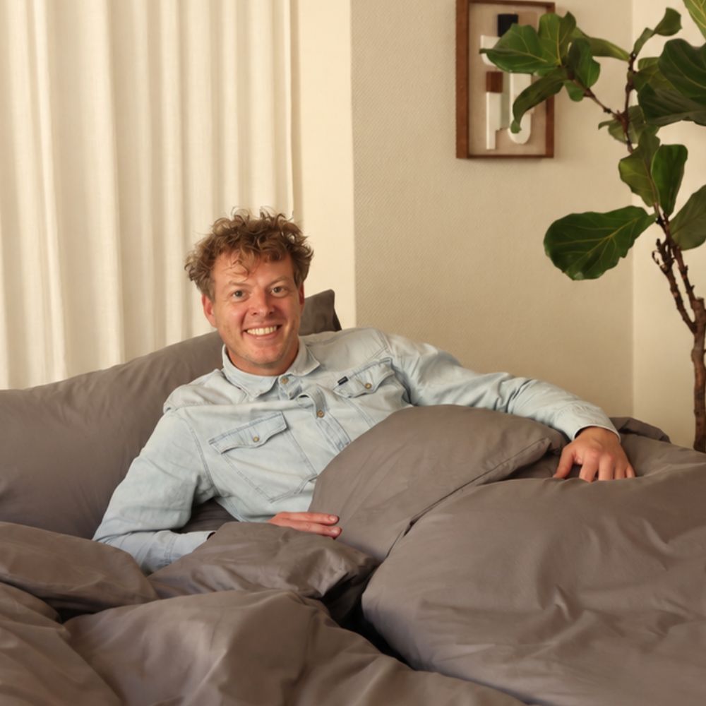 Plumelle washable duvet in Warm Grey with a man relaxing in bed, seamless one-piece cotton duvet with built-in cover in a bright minimalist bedroom
